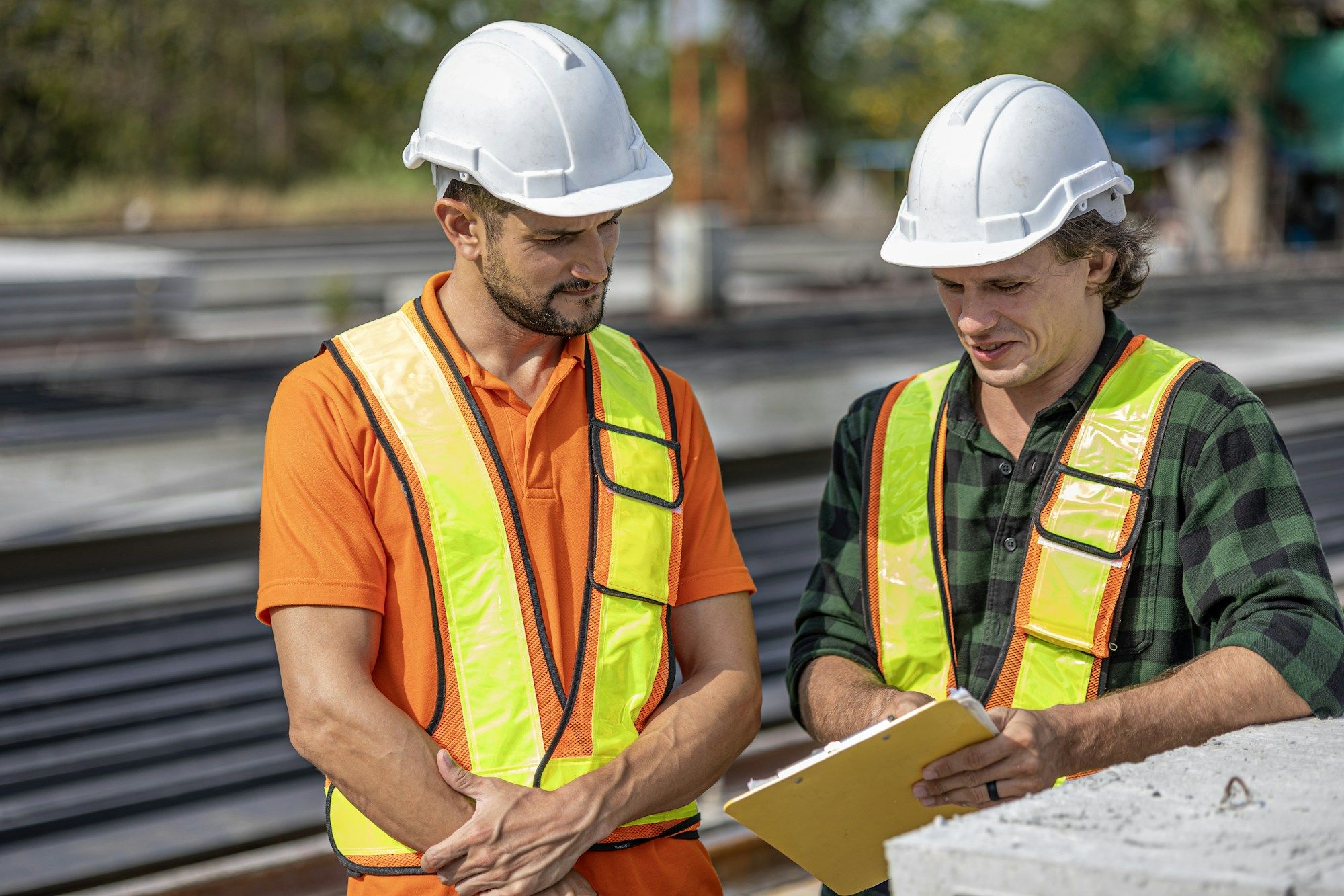 Two site workers in hard hats and high-visibility vests reviewing safety paperwork on a job site